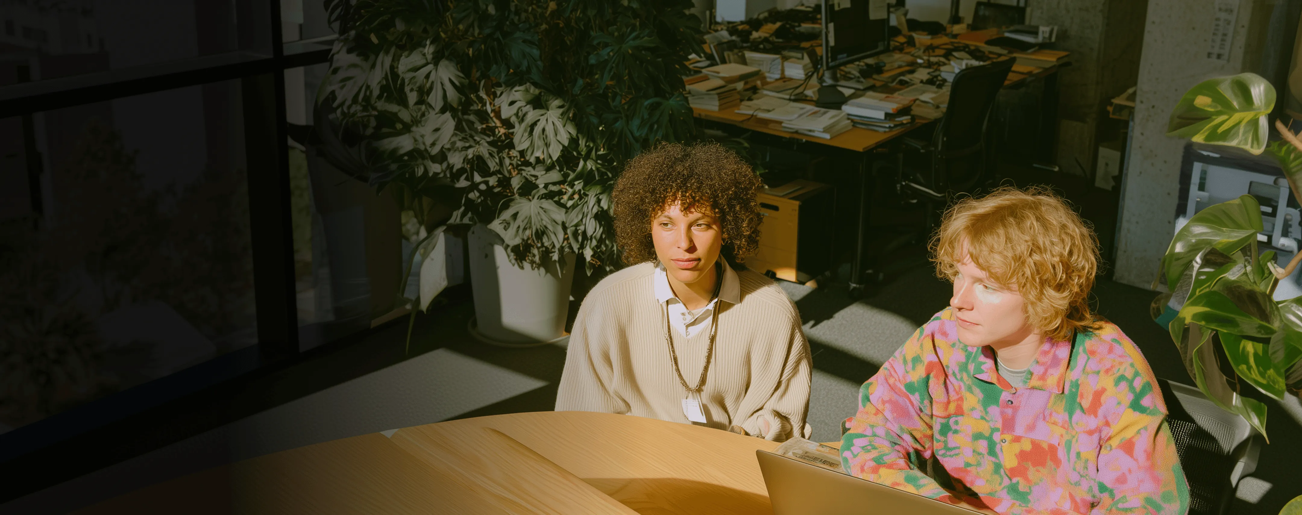 Zwei Personen an einem Schreibtisch in einem sonnigen Büro, die aufmerksam zuhören